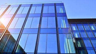 Cam cepheli modern ofis binası. Ofis binasının şeffaf cam duvarı. Binanın ön cephesinde mavi gökyüzünün yansıması.