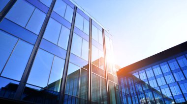 Cam cepheli modern ofis binası. Ofis binasının şeffaf cam duvarı. Binanın ön cephesinde mavi gökyüzünün yansıması.