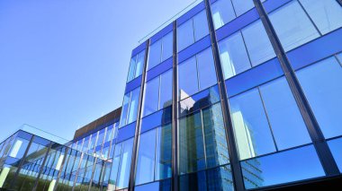 Cam cepheli modern ofis binası. Ofis binasının şeffaf cam duvarı. Binanın ön cephesinde mavi gökyüzünün yansıması.