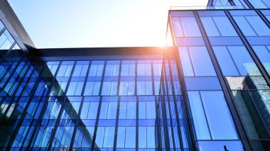 Cam cepheli modern ofis binası. Ofis binasının şeffaf cam duvarı. Binanın ön cephesinde mavi gökyüzünün yansıması.