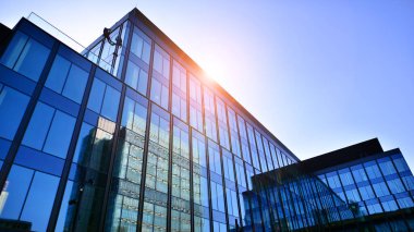 Cam cepheli modern ofis binası. Ofis binasının şeffaf cam duvarı. Binanın ön cephesinde mavi gökyüzünün yansıması.