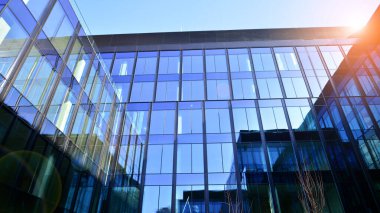 Cam cepheli modern ofis binası. Ofis binasının şeffaf cam duvarı. Binanın ön cephesinde mavi gökyüzünün yansıması.