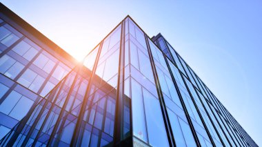 Cam cepheli modern ofis binası. Ofis binasının şeffaf cam duvarı. Binanın ön cephesinde mavi gökyüzünün yansıması.