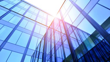 Cam cepheli modern ofis binası. Ofis binasının şeffaf cam duvarı. Binanın ön cephesinde mavi gökyüzünün yansıması.