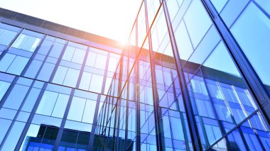 Cam cepheli modern ofis binası. Ofis binasının şeffaf cam duvarı. Binanın ön cephesinde mavi gökyüzünün yansıması.