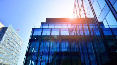 Cam cepheli modern ofis binası. Ofis binasının şeffaf cam duvarı. Binanın ön cephesinde mavi gökyüzünün yansıması.