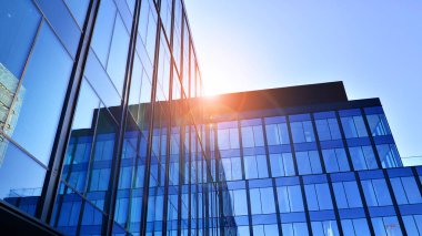 Cam cepheli modern ofis binası. Ofis binasının şeffaf cam duvarı. Binanın ön cephesinde mavi gökyüzünün yansıması.