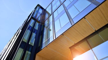 Cam cepheli modern ofis binası. Ofis binasının şeffaf cam duvarı. Binanın ön cephesinde mavi gökyüzünün yansıması.