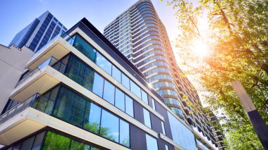 Çevre mimarisi. Yeşil ağaç ve yeni konut binası. Doğanın ve modernliğin ahengi. Yeşil yerleşim bölgesinde yeni daireleri olan modern bir apartman..