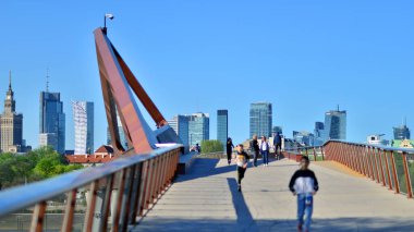 Varşova, Polonya. 11 Nisan 2024. Vistula Nehri üzerindeki köprü sadece yayalar ve bisikletçiler içindir. Arka planda, gökdelenleri olan bir şehir manzarası var..