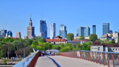 Varşova, Polonya. 11 Nisan 2024. Vistula Nehri üzerindeki köprü sadece yayalar ve bisikletçiler içindir. Arka planda, gökdelenleri olan bir şehir manzarası var..
