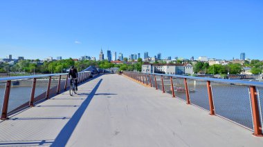 Varşova, Polonya. 11 Nisan 2024. Vistula Nehri üzerindeki köprü sadece yayalar ve bisikletçiler içindir. Arka planda, gökdelenleri olan bir şehir manzarası var..