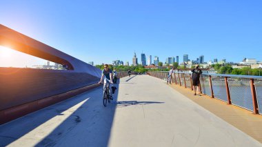 Varşova, Polonya. 11 Nisan 2024. Vistula Nehri üzerindeki köprü sadece yayalar ve bisikletçiler içindir. Arka planda, gökdelenleri olan bir şehir manzarası var..