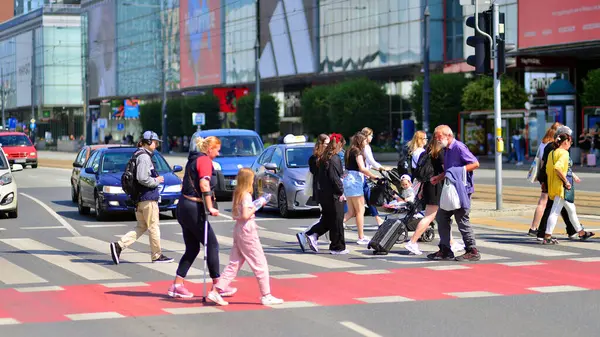 Varşova, Polonya. 8 Haziran 2024. Büyük bir şehrin caddesi. Farklı yaşlarda insanlar karşıdan karşıya geçiyor. Şehir caddesi manzarası sakinleri, turistler ve modern binalar. Şehir merkezinde güneşli bir günde.