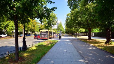 Varşova, Polonya. 9 Temmuz 2024. Şehirde yaz. Şehir merkezindeki işlek bir caddenin arka planında parlak güneş ışığıyla şehir kaldırımında yürüyen insanlar..