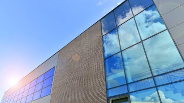 Çelik ve camdan yapılmış modern bir binanın parçası. Soyut modern ticari mimari parçası. Mavi gökyüzünün altında parlak camdan ve çelikten duvarlar.