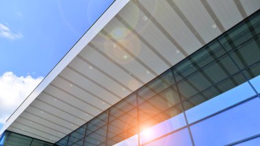 Çelik ve camdan yapılmış modern bir binanın parçası. Soyut modern ticari mimari parçası. Mavi gökyüzünün altında parlak camdan ve çelikten duvarlar.