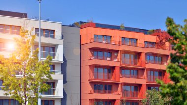 Bir sürü balkon ve penceresi olan bir apartman. Bina ağaçlarla çevrili ve bir sürü yeşilliği var. Binaların çevresi yeşildir. Ekolojik konutlar.