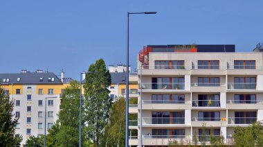 Bir sürü balkon ve penceresi olan bir apartman. Bina ağaçlarla çevrili ve bir sürü yeşilliği var. Binaların çevresi yeşildir. Ekolojik konutlar.
