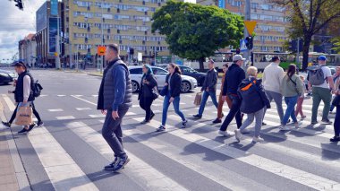 Szczecin, Polonya. 14 Eylül 2024. Şehir merkezinde güneşli bir günde ve büyük bir şehrin caddesinde. Farklı yaşlarda insanlar karşıdan karşıya geçiyor. Şehir sakinleri ve modern binaların olduğu bir cadde manzarası.