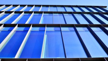 Mavi gökyüzüne karşı birçok penceresi olan modern binanın dış görünüşü, düşük açı görünümü.