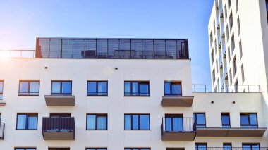 Beyaz, modern, yüksek katlı apartman binası, mavi gökyüzüne karşı dik dur, parlak, açısal tasarımlarla yenilikçi şehir mimarisini örnek al..