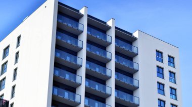 Beyaz, modern, yüksek katlı apartman binası, mavi gökyüzüne karşı dik dur, parlak, açısal tasarımlarla yenilikçi şehir mimarisini örnek al..