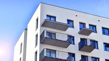 Beyaz, modern, yüksek katlı apartman binası, mavi gökyüzüne karşı dik dur, parlak, açısal tasarımlarla yenilikçi şehir mimarisini örnek al..