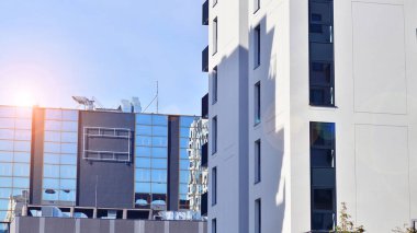 Beyaz, modern, yüksek katlı apartman binası, mavi gökyüzüne karşı dik dur, parlak, açısal tasarımlarla yenilikçi şehir mimarisini örnek al..