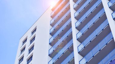 Beyaz, modern, yüksek katlı apartman binası, mavi gökyüzüne karşı dik dur, parlak, açısal tasarımlarla yenilikçi şehir mimarisini örnek al..