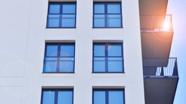 Beyaz, modern, yüksek katlı apartman binası, mavi gökyüzüne karşı dik dur, parlak, açısal tasarımlarla yenilikçi şehir mimarisini örnek al..