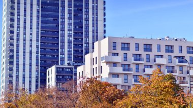 Beyaz, modern, yüksek katlı apartman binası, mavi gökyüzüne karşı dik dur, parlak, açısal tasarımlarla yenilikçi şehir mimarisini örnek al..