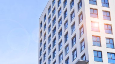 Beyaz, modern, yüksek katlı apartman binası, mavi gökyüzüne karşı dik dur, parlak, açısal tasarımlarla yenilikçi şehir mimarisini örnek al..