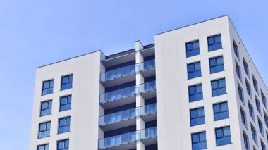 Beyaz, modern, yüksek katlı apartman binası, mavi gökyüzüne karşı dik dur, parlak, açısal tasarımlarla yenilikçi şehir mimarisini örnek al..