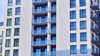 Beyaz, modern, yüksek katlı apartman binası, mavi gökyüzüne karşı dik dur, parlak, açısal tasarımlarla yenilikçi şehir mimarisini örnek al..