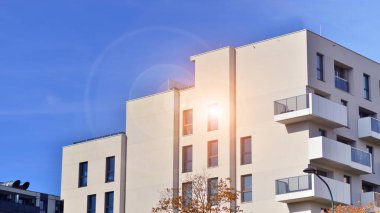 Beyaz, modern, yüksek katlı apartman binası, mavi gökyüzüne karşı dik dur, parlak, açısal tasarımlarla yenilikçi şehir mimarisini örnek al..