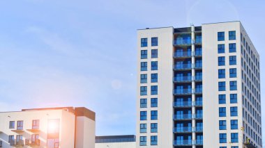 Beyaz, modern, yüksek katlı apartman binası, mavi gökyüzüne karşı dik dur, parlak, açısal tasarımlarla yenilikçi şehir mimarisini örnek al..