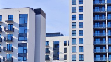 Beyaz, modern, yüksek katlı apartman binası, mavi gökyüzüne karşı dik dur, parlak, açısal tasarımlarla yenilikçi şehir mimarisini örnek al..