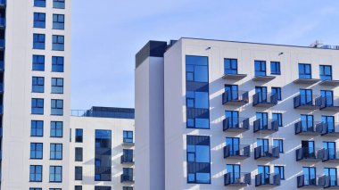 Beyaz, modern, yüksek katlı apartman binası, mavi gökyüzüne karşı dik dur, parlak, açısal tasarımlarla yenilikçi şehir mimarisini örnek al..
