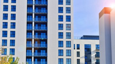 Beyaz, modern, yüksek katlı apartman binası, mavi gökyüzüne karşı dik dur, parlak, açısal tasarımlarla yenilikçi şehir mimarisini örnek al..