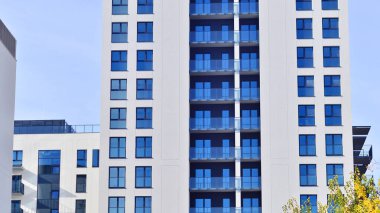 Beyaz, modern, yüksek katlı apartman binası, mavi gökyüzüne karşı dik dur, parlak, açısal tasarımlarla yenilikçi şehir mimarisini örnek al..