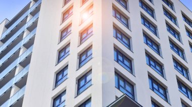 Beyaz, modern, yüksek katlı apartman binası, mavi gökyüzüne karşı dik dur, parlak, açısal tasarımlarla yenilikçi şehir mimarisini örnek al..