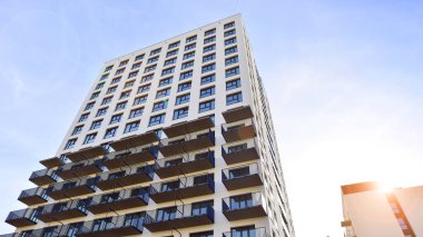 Beyaz, modern, yüksek katlı apartman binası, mavi gökyüzüne karşı dik dur, parlak, açısal tasarımlarla yenilikçi şehir mimarisini örnek al..
