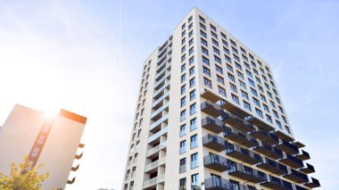 Beyaz, modern, yüksek katlı apartman binası, mavi gökyüzüne karşı dik dur, parlak, açısal tasarımlarla yenilikçi şehir mimarisini örnek al..