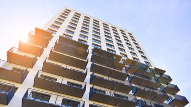 Beyaz, modern, yüksek katlı apartman binası, mavi gökyüzüne karşı dik dur, parlak, açısal tasarımlarla yenilikçi şehir mimarisini örnek al..