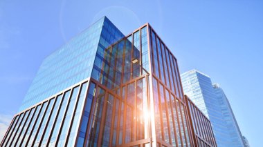 Arka planda mavi gökyüzü olan modern yüksek katlı ofis binalarına bakıyorum..