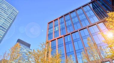 Arka planda mavi gökyüzü olan modern yüksek katlı ofis binalarına bakıyorum..