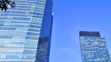 Arka planda mavi gökyüzü olan modern yüksek katlı ofis binalarına bakıyorum..