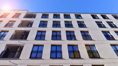 Mavi gökyüzü olan güneşli bir günde modern apartman binaları. Modern bir apartmanın ön cephesi. Güneş ışığıyla kaplı cam yüzey..
