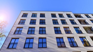 Mavi gökyüzü olan güneşli bir günde modern apartman binaları. Modern bir apartmanın ön cephesi. Güneş ışığıyla kaplı cam yüzey..